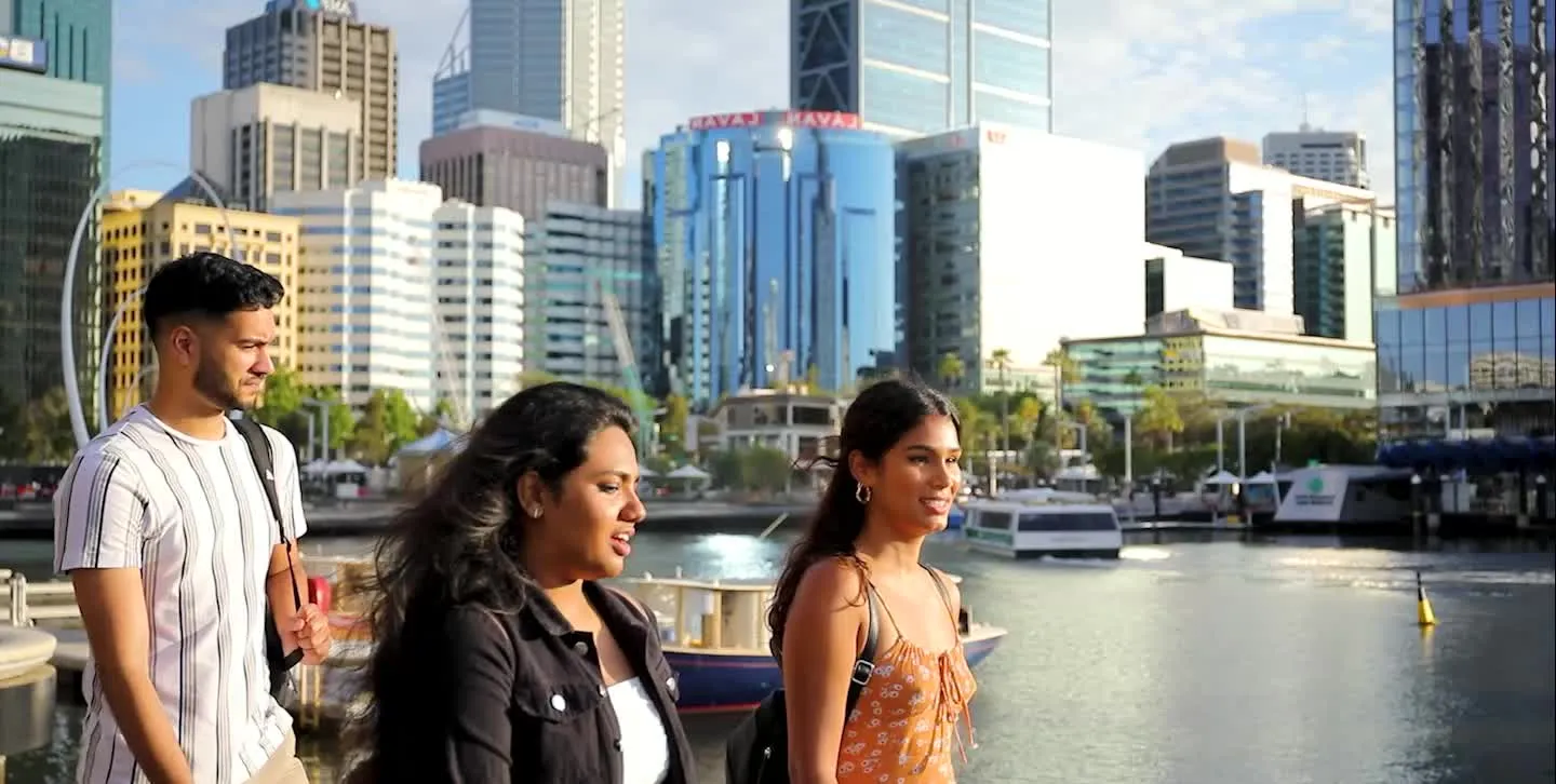 Three Kaplan Business School students walking together with the Perth city skyline behind them