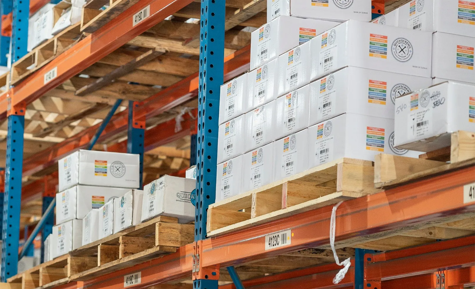 QuickScrews branded boxes stacked on orange warehouse racking in the company's distribution center